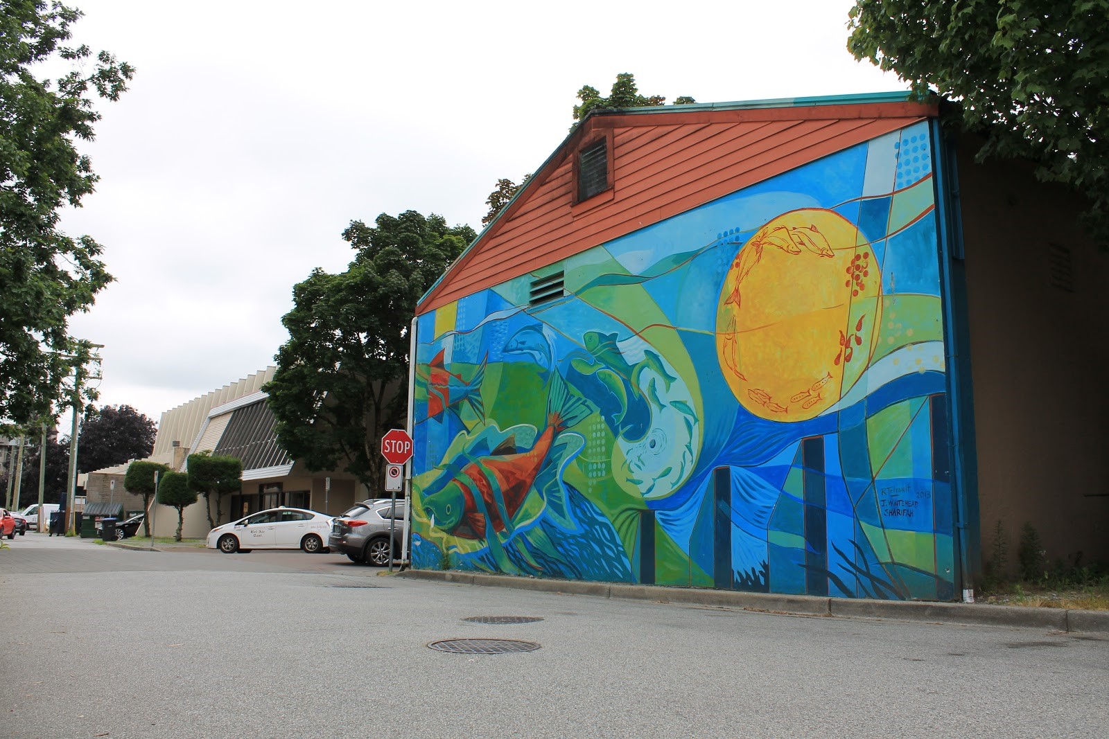 A photograph of the salmon cycle mural in Leigh Square. It contains a sun-like circle, showing the development from eggs, to fry, to small fish, to adult fish, as well as colourful adult fish swimming in the river.