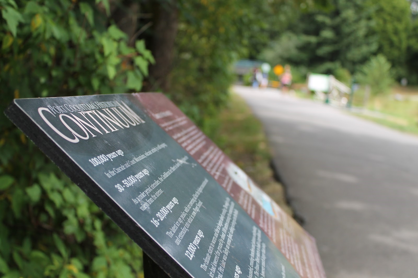 A close-up photo of a Port Coquitlam Heritage Continuum sign on the side of a tree-lined trail.