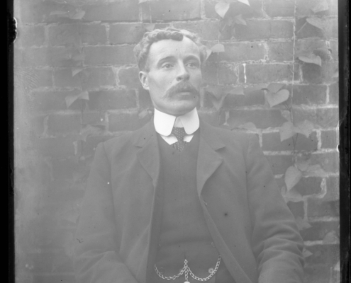 Black and white photo of a man wearing a suit seated in front of a brick wall, facing the camera