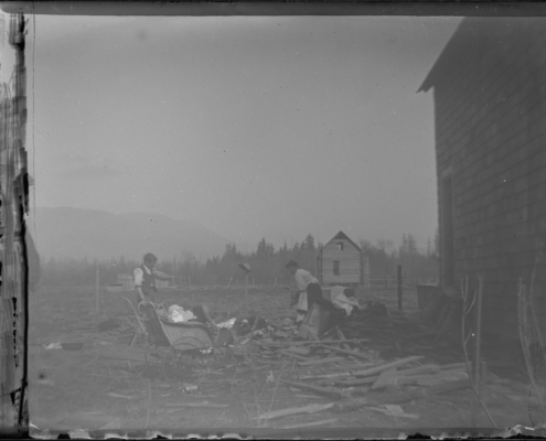 Black and white photo of two men standing beside a house sorting through indistinguishable rubble