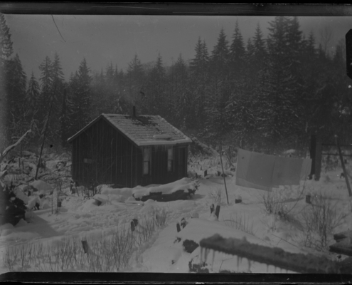 Black and white photo of a small wooden cabin surrounded by trees and snow