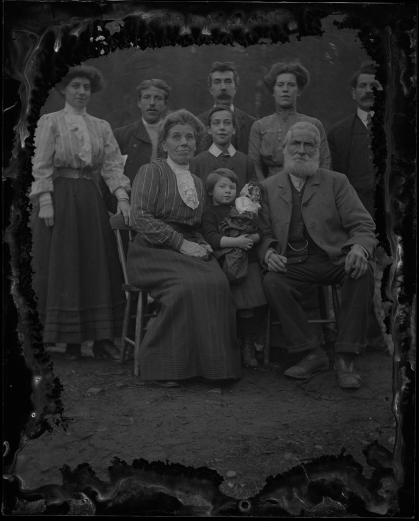 A posed, black and white family photo of five adults standing behind an elderly couple seated on chairs. Two children stand between them