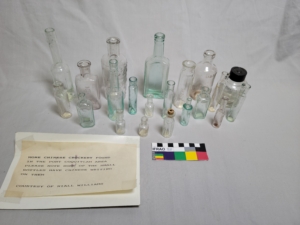 Twenty-one small glass bottles of various shapes and sizes arranged on a table