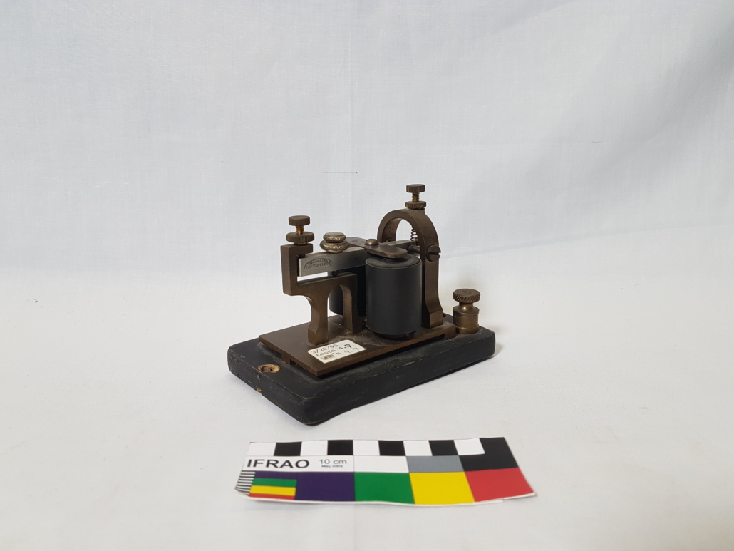 A small metal telegraph machine with two barrels on a black wooden base