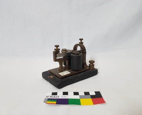A small metal telegraph machine with two barrels on a black wooden base