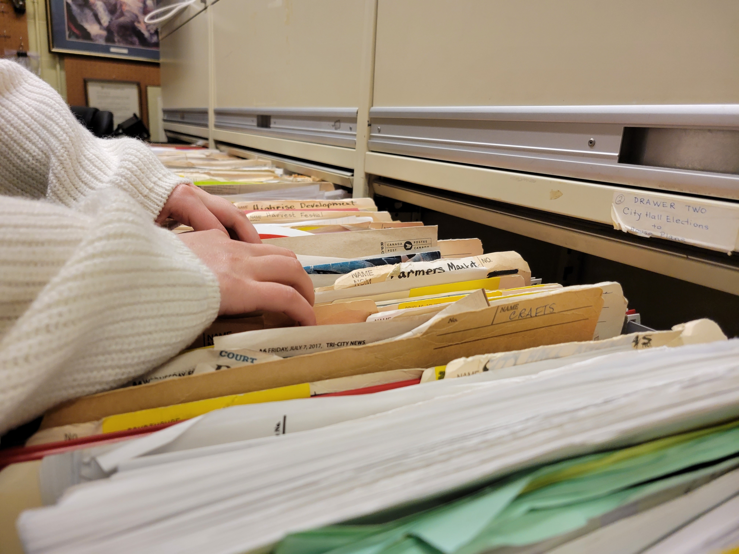 A closeup of a person's hands sorting through drawers of crowded stand-up files