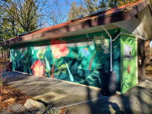 A picture of the Rain Garden mural on the side of the building. It has foliage and bright flowers, as well as comically large raindrops.