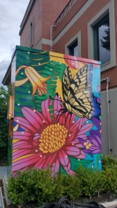 An electrical box decorated with a bright garden scene of flowers and butterflies.