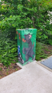 A smaller electrical box decorated with art of a bear in a forest. 